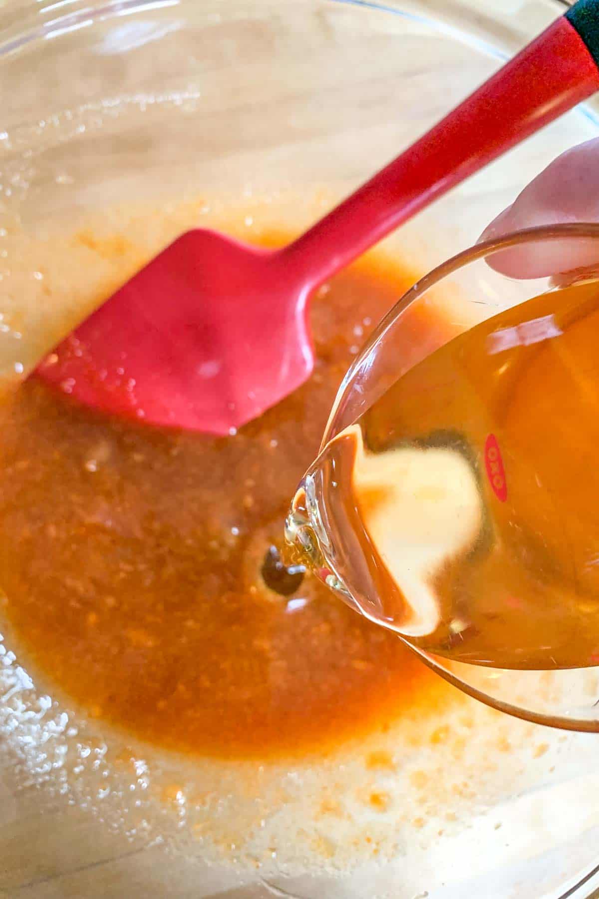 Vegetable oil being poured into a glass mixing bowl.