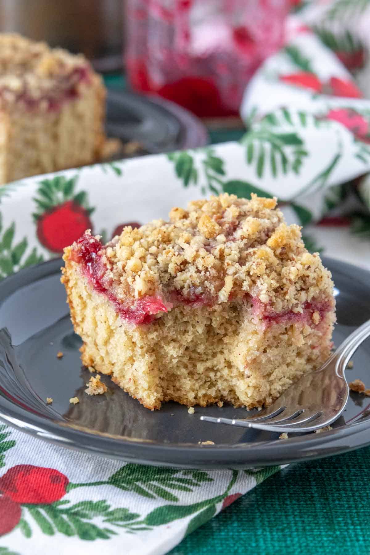 Slice of cranberry coffee cake on a black plate with a bite taken.