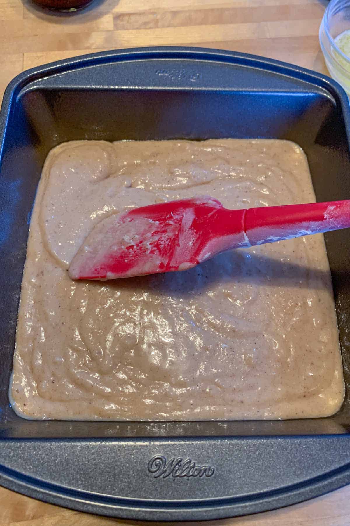 Spreading coffee cake batter into a baking pan with a spatula.
