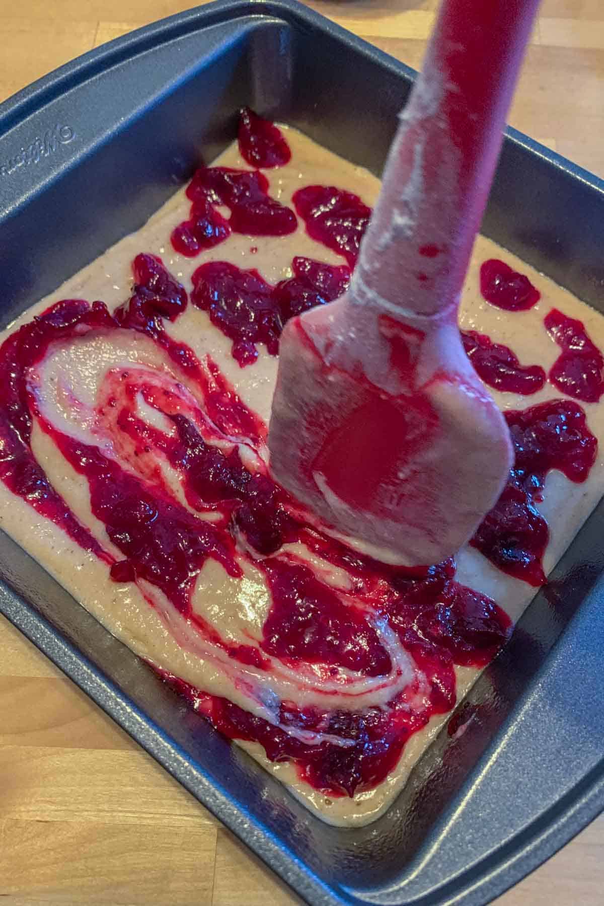 Swirling cranberry sauce into coffee cake batter with a spatula.