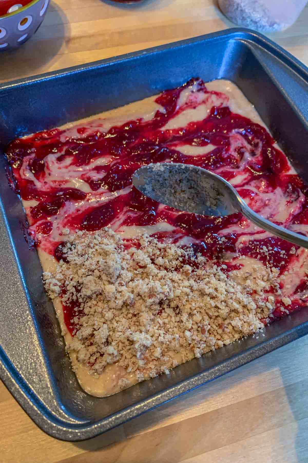 Spooning streusel topping onto cranberry coffee cake.