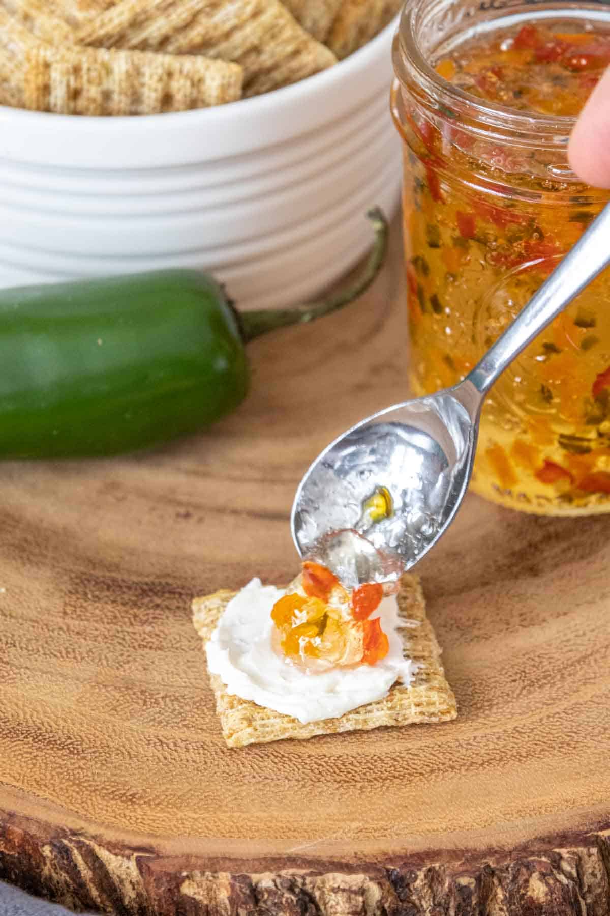 Spooning pepper jelly onto a cracker with cream cheese.