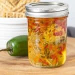 Jar of jalapeño jelly on a wood tray with a jalapeño and crackers behind.