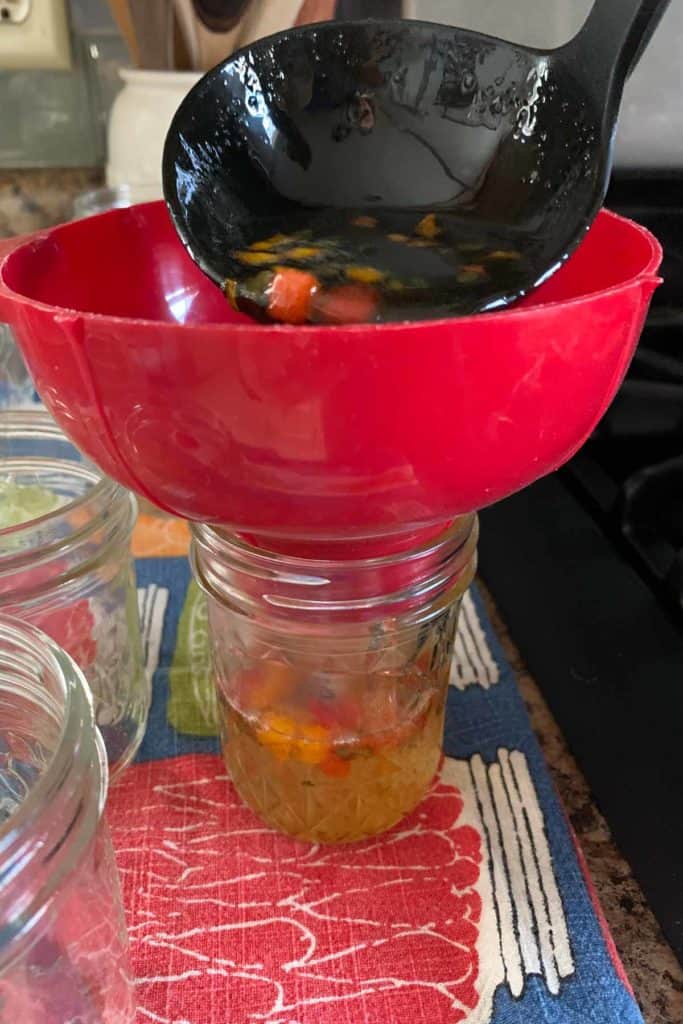 Ladling pepper jelly into jars with a funnel on the jar.