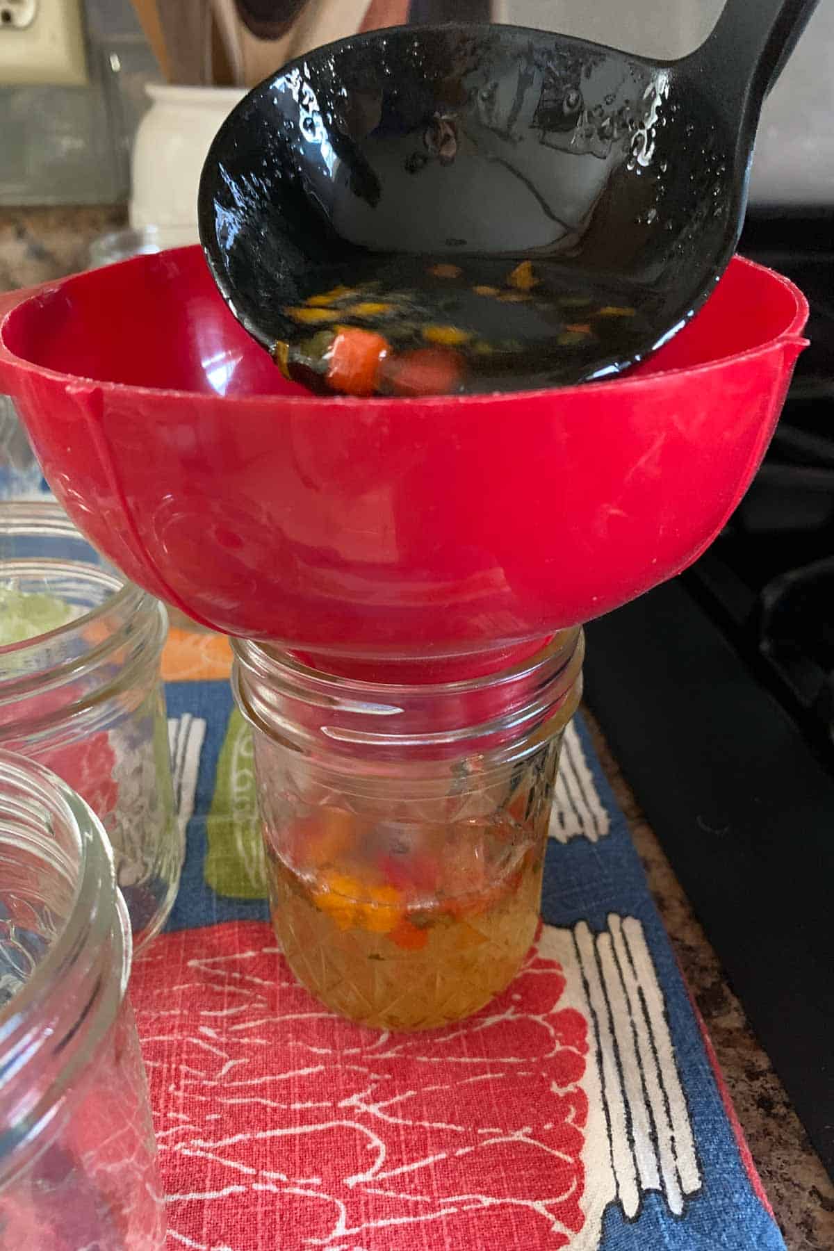 Ladling pepper jelly into jars with a funnel on the jar.