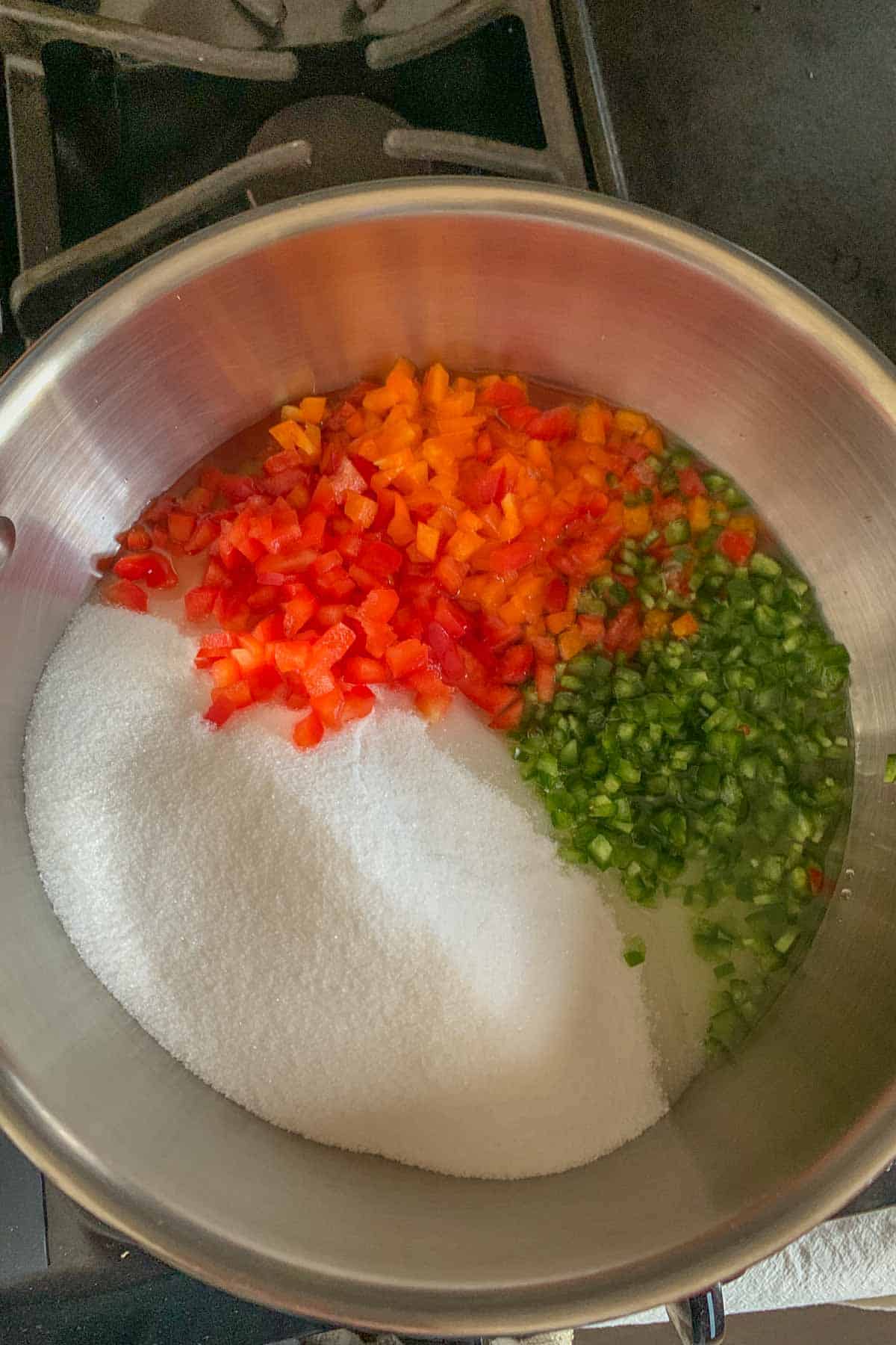 Sugar, jalapeños, bell peppers, and vinegar in a stainless pan.