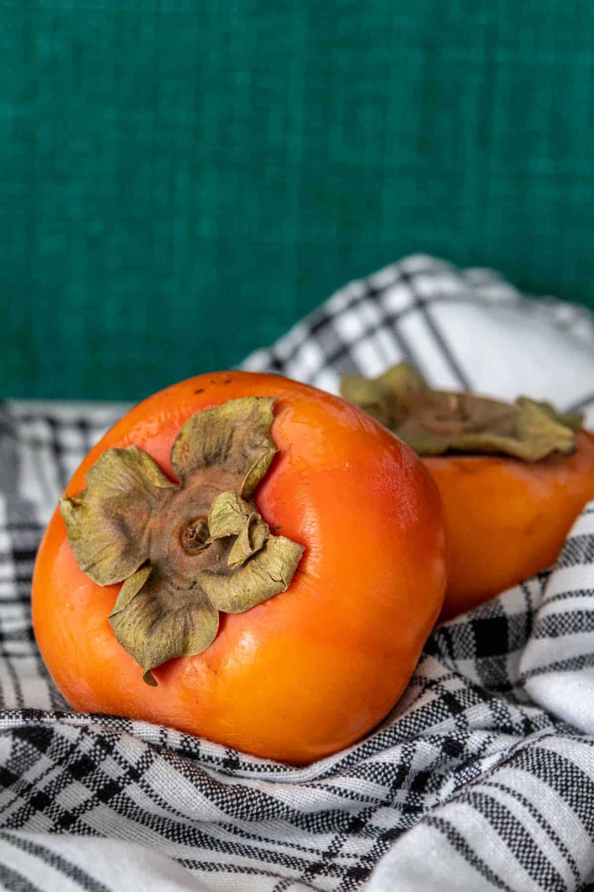 Persimmons on a black and white plaid napkin with a green wall behind.