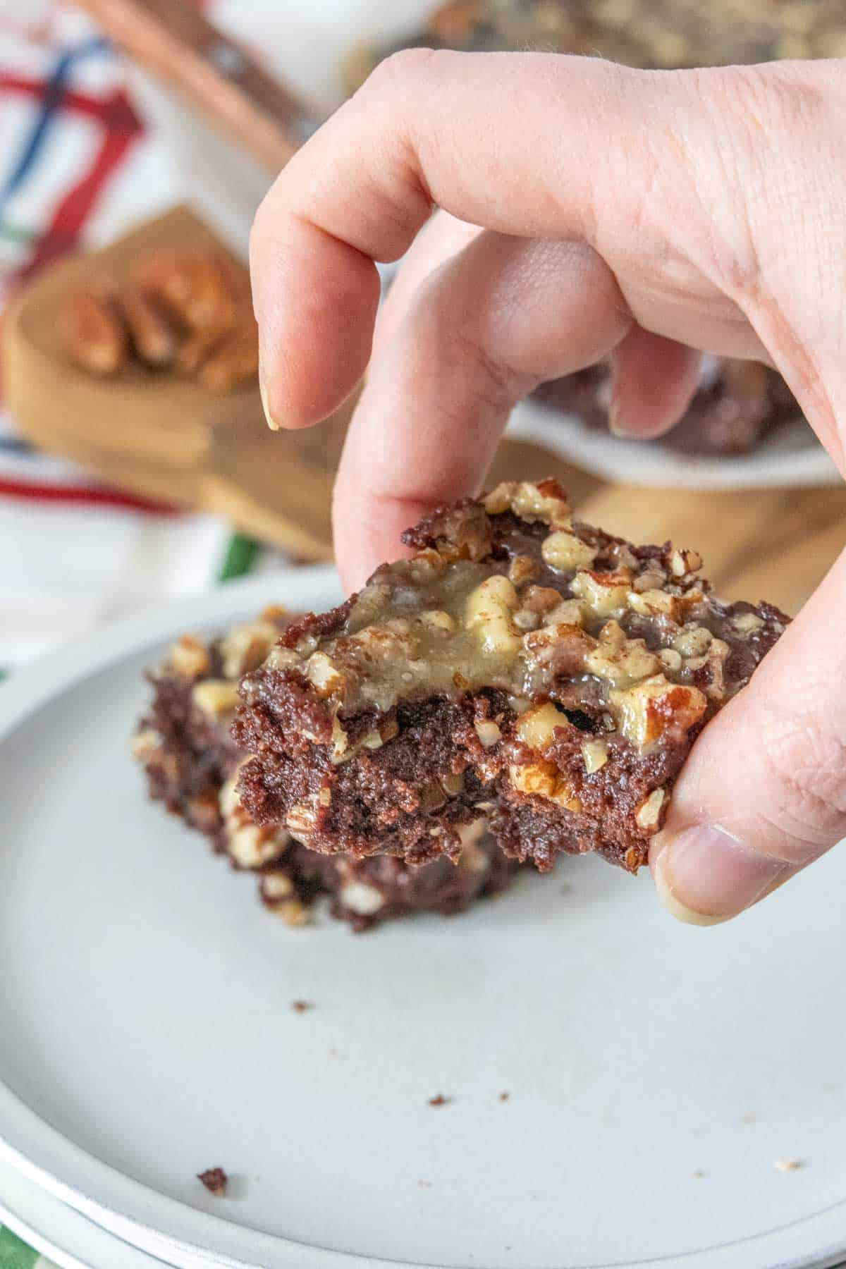 Caucasian hand holding a turtle brownie with a bite taken, showing fudgy interior.
