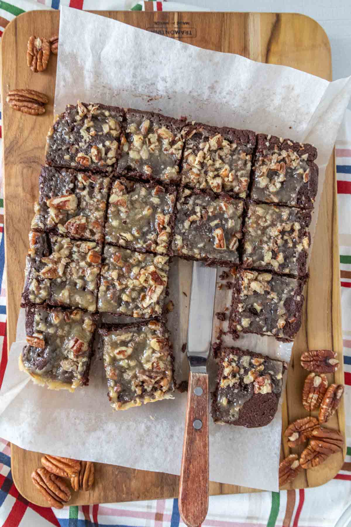 Overhead of a cut batch of turtle brownies with pecans and an offset spatula.