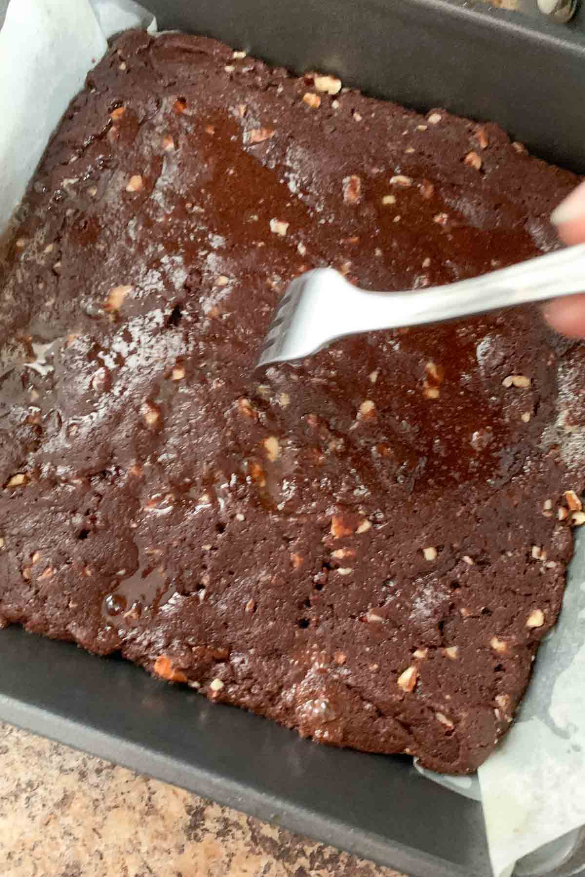 Using a fork to poke holes in parbaked turtle brownies.