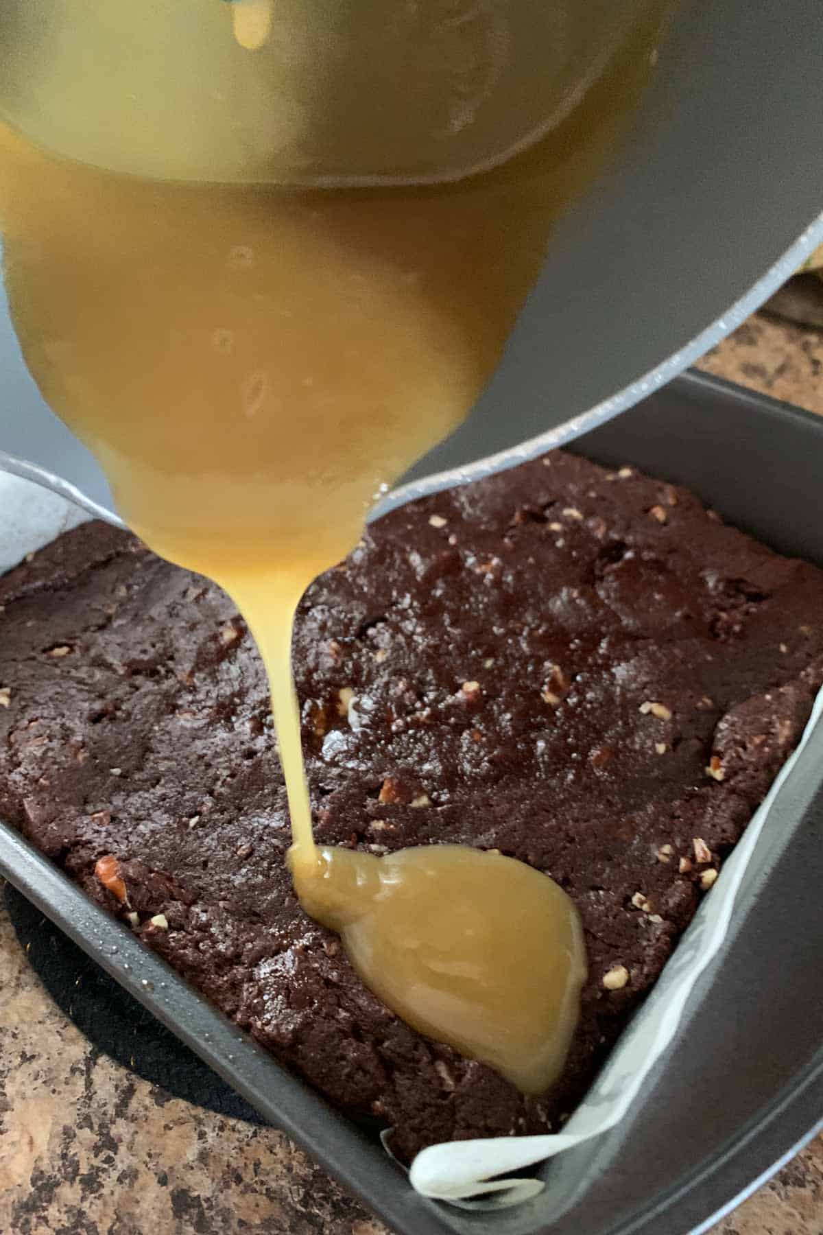 Pouring butterscotch sauce over parbaked brownies.