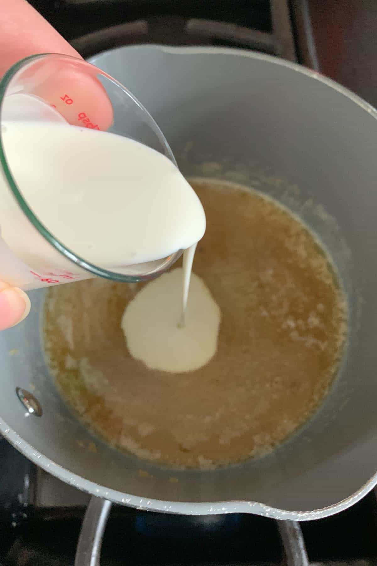 Pouring cream into melted butter and sugar in a saucepan to make butterscotch sauce.