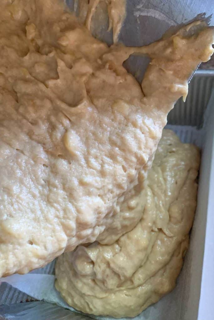 Banana bread batter being poured into a loaf pan.