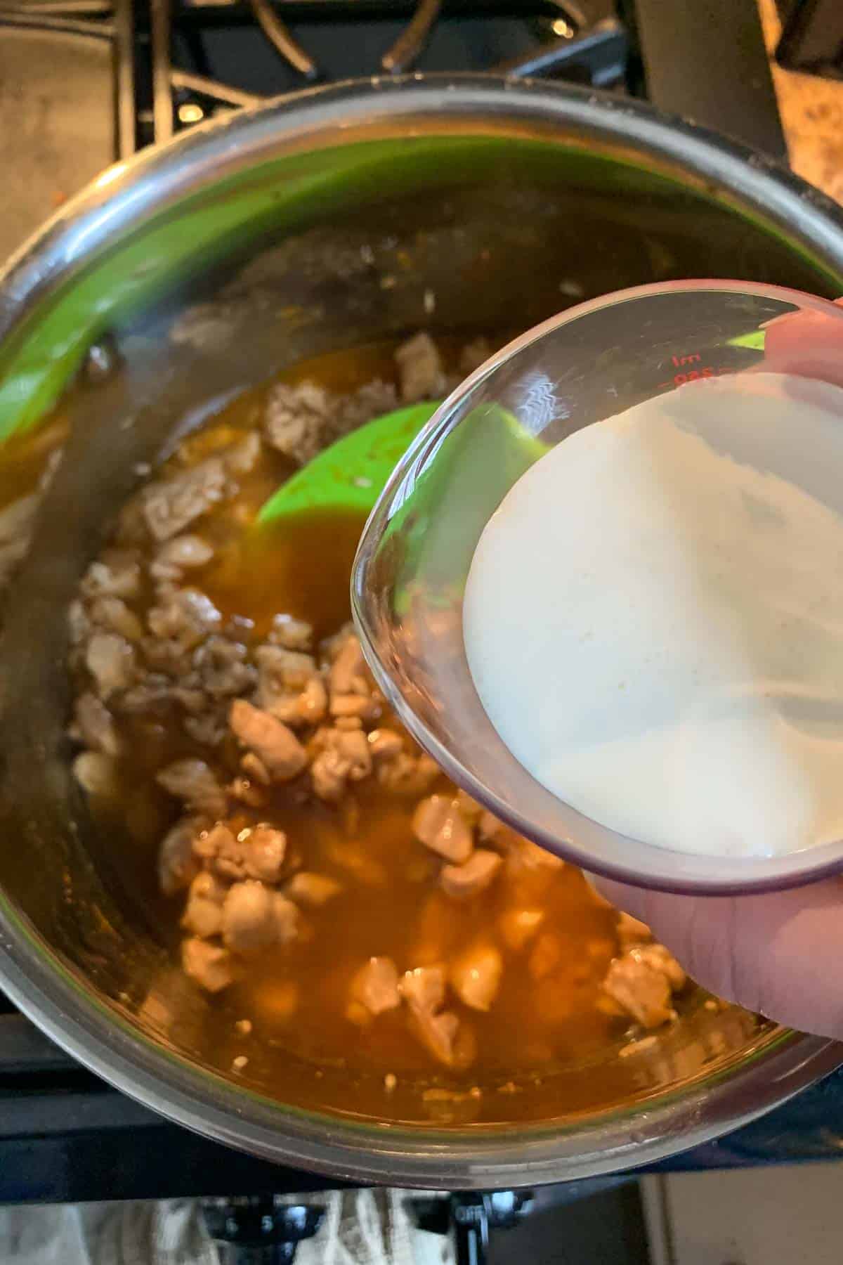 Adding cream to cooked chicken and broth in stock pot.
