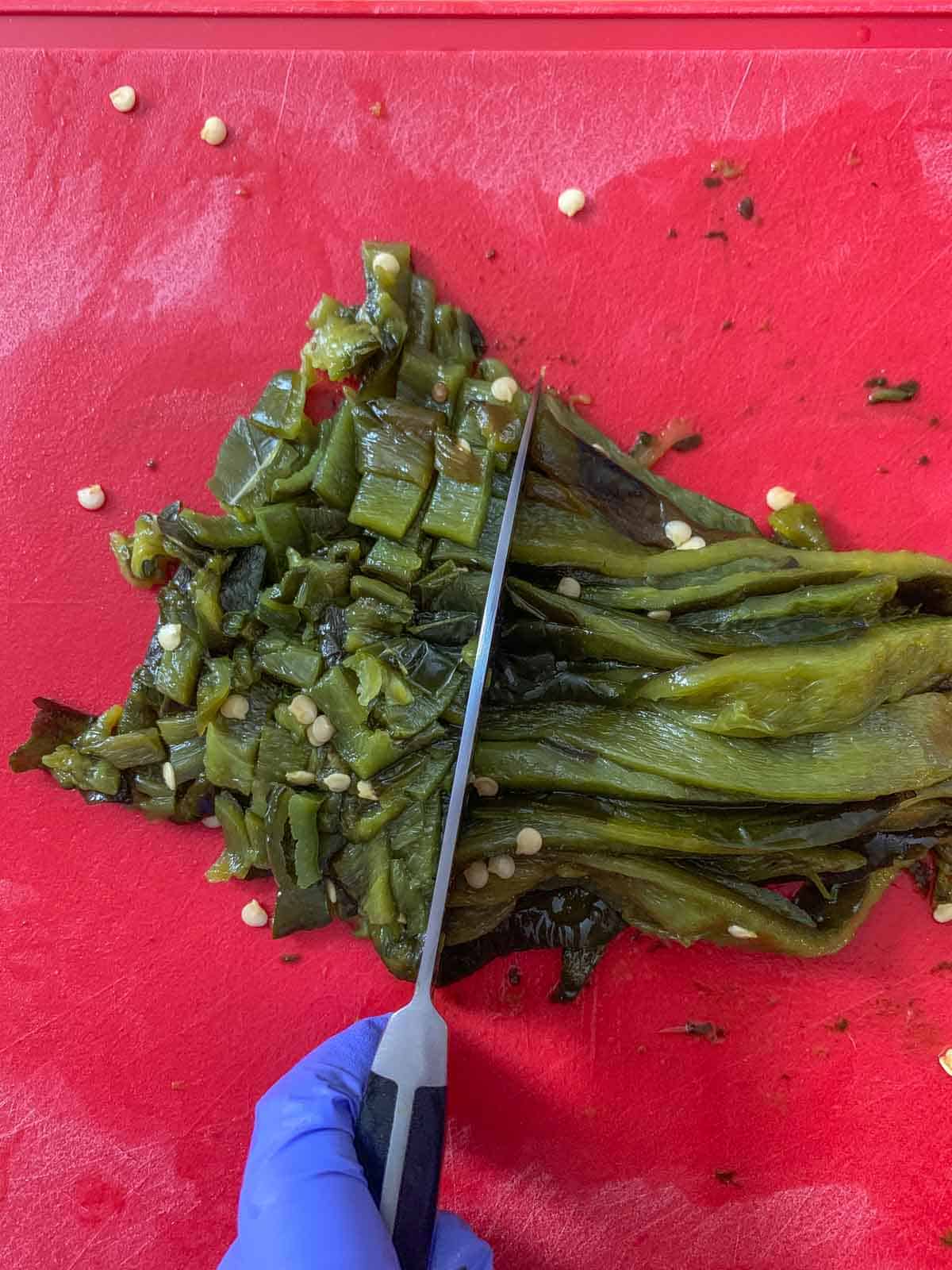 Roasted poblano peppers on a cutting board being chopped.