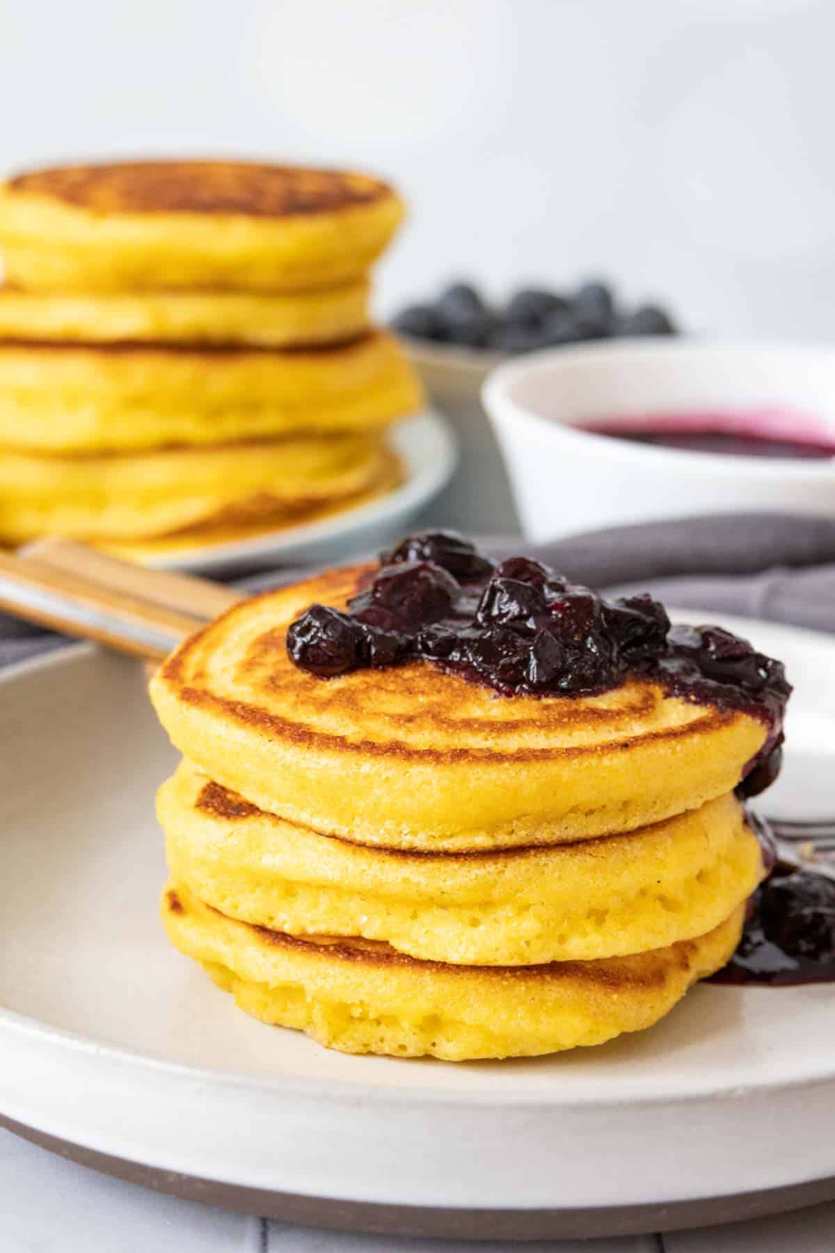 Stack of cornmeal pancakes with blueberry sauce spilling down the side.