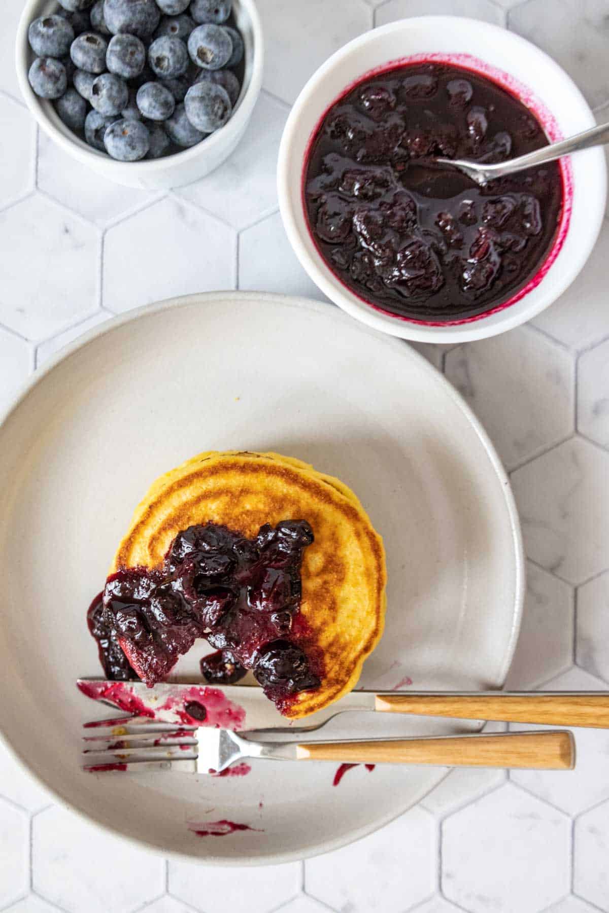 Overhead of cornmeal pancakes with blueberry sauce, partially eaten.
