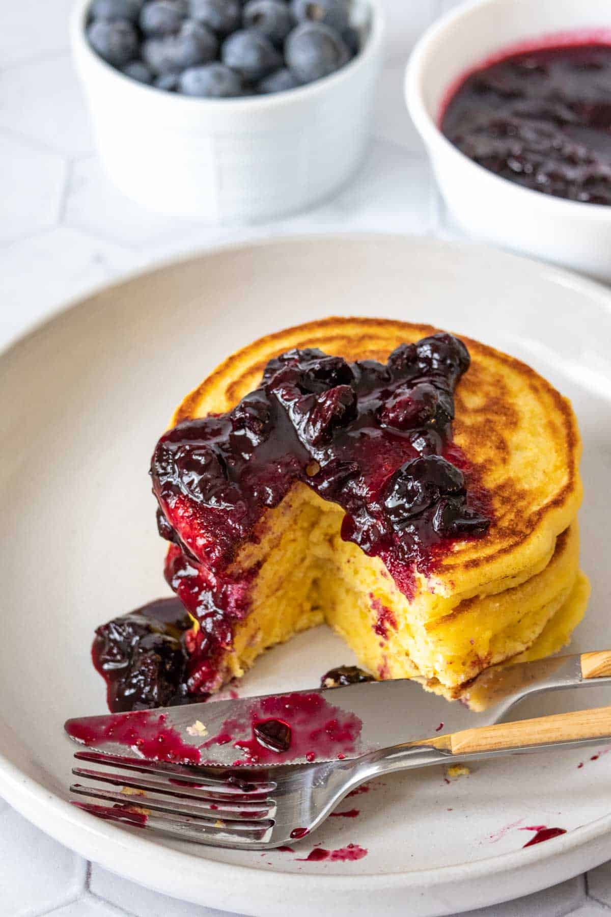 Cornmeal pancakes on a plate with blueberry sauce, partially eaten.