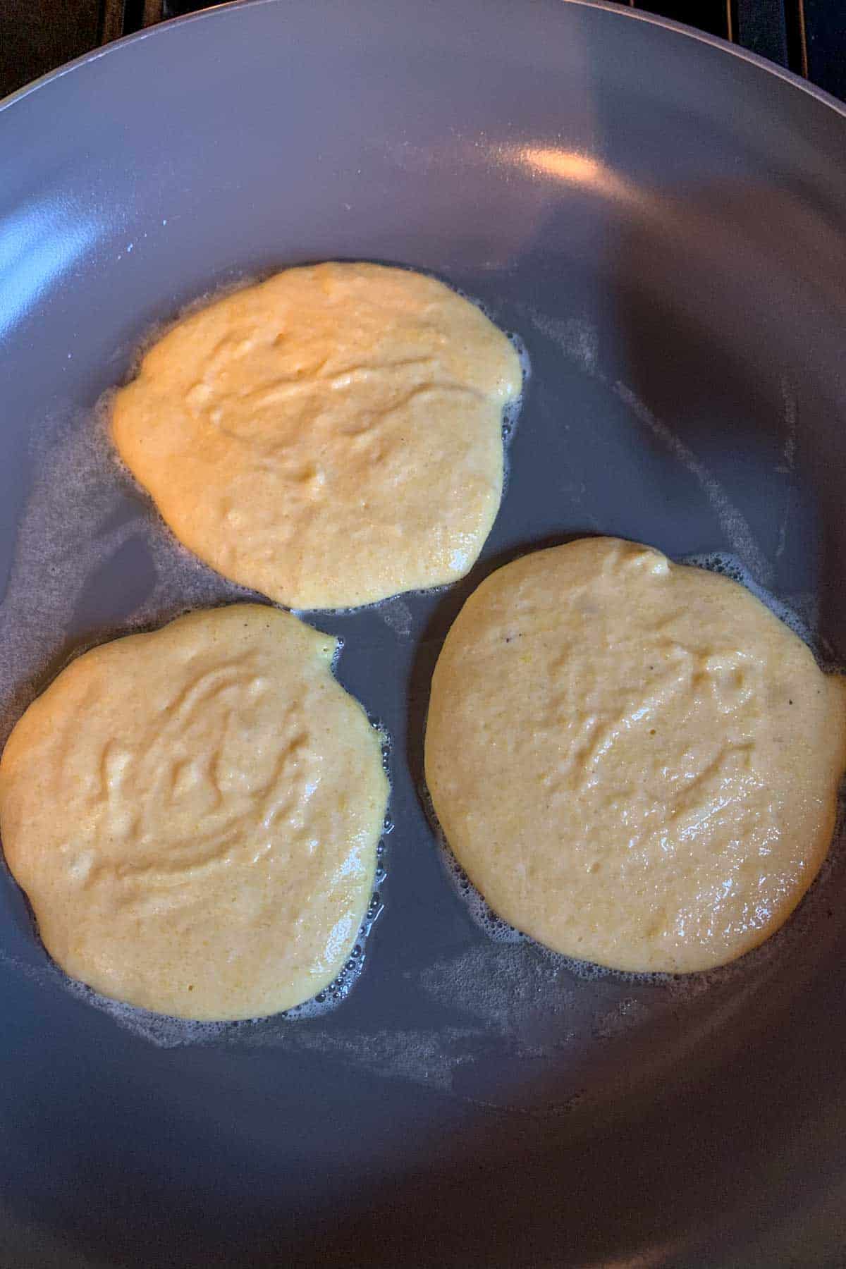 Cornmeal pancakes in a saute pan cooking.