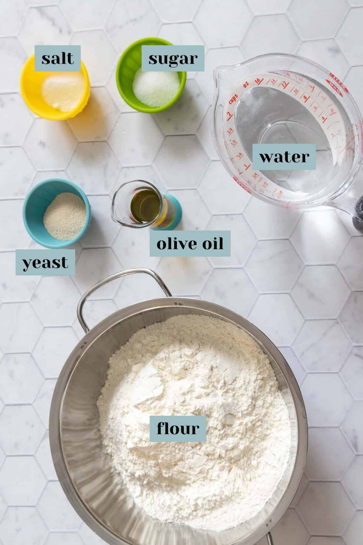 Ingredients for French bread on a tile surface with labels.