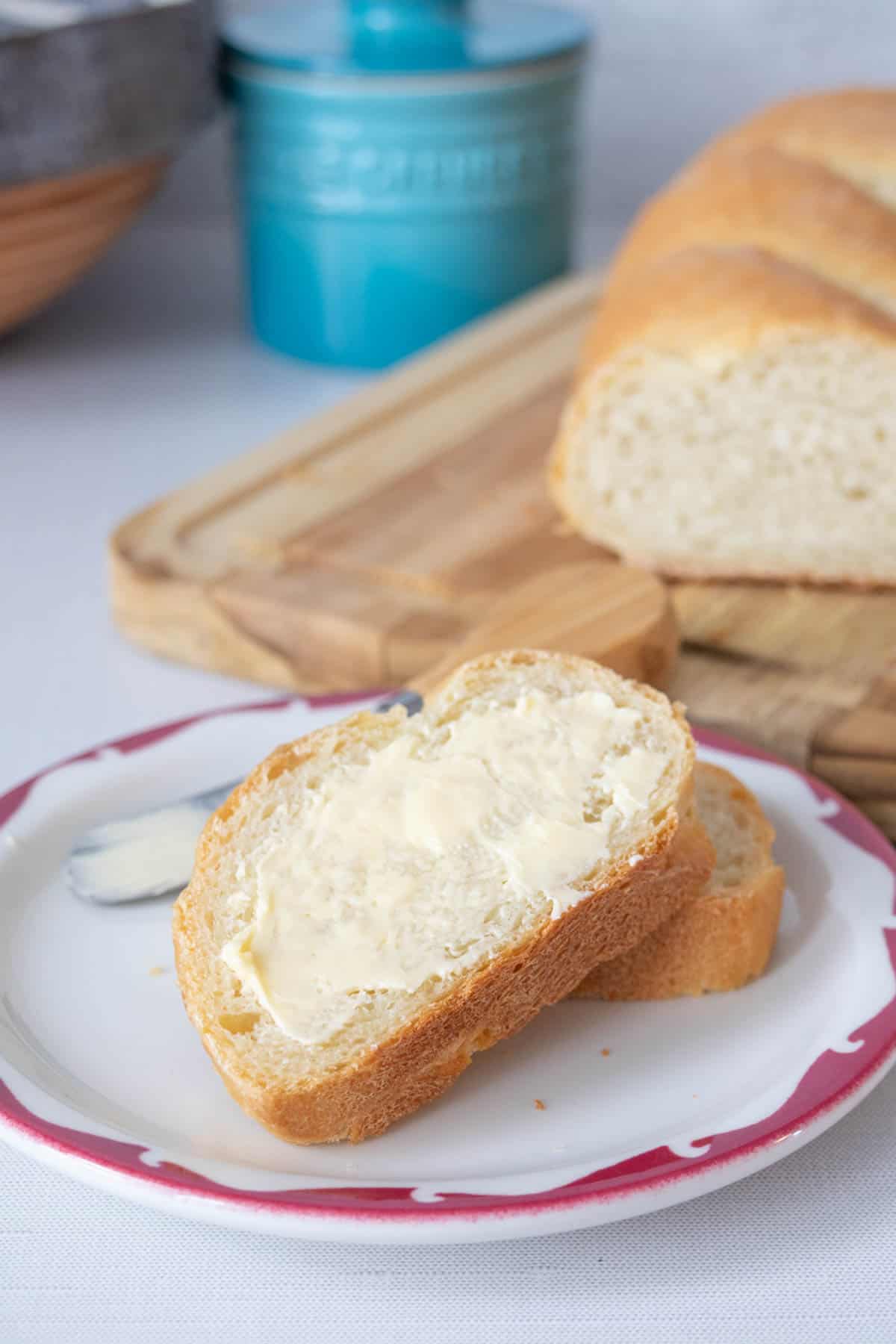 Two slices of French bread stacked on a plate with butter on the top slice.