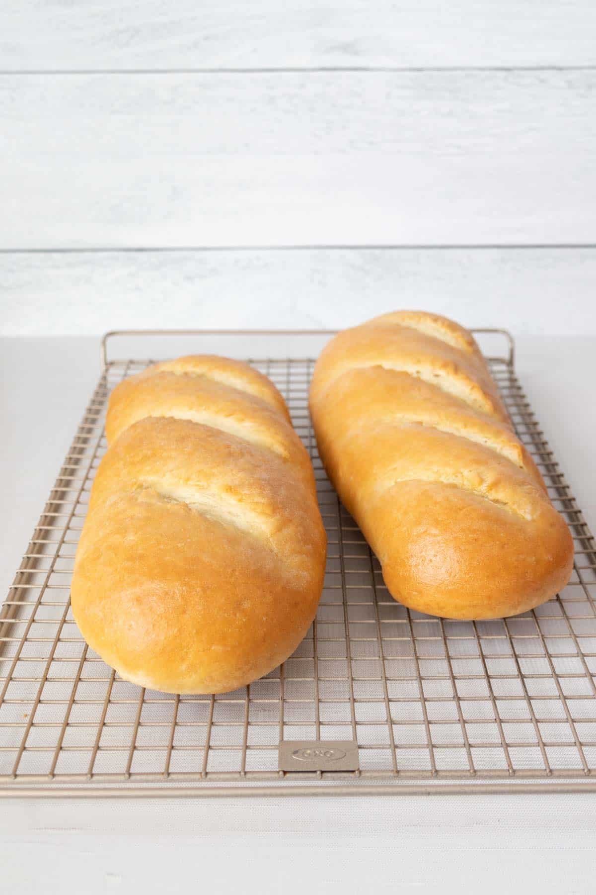Two baked loaves of French bread on a wire cooling rack.