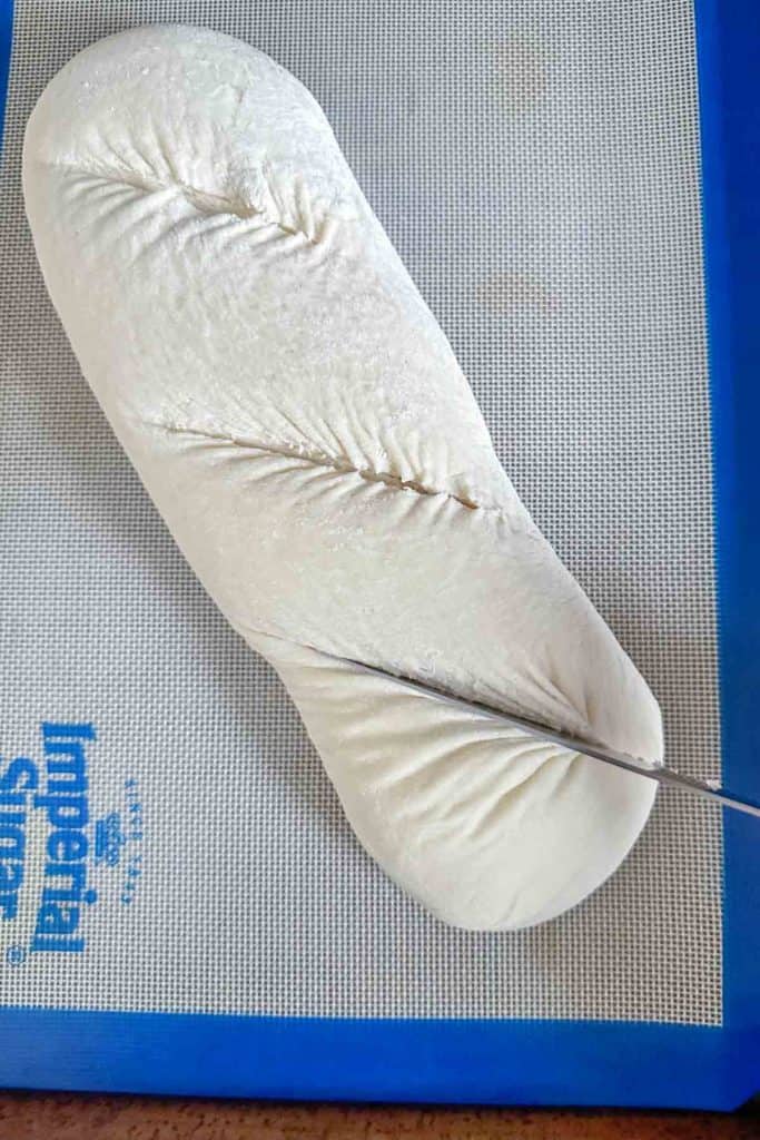 Using a knife to cut slashes into unbaked bread.