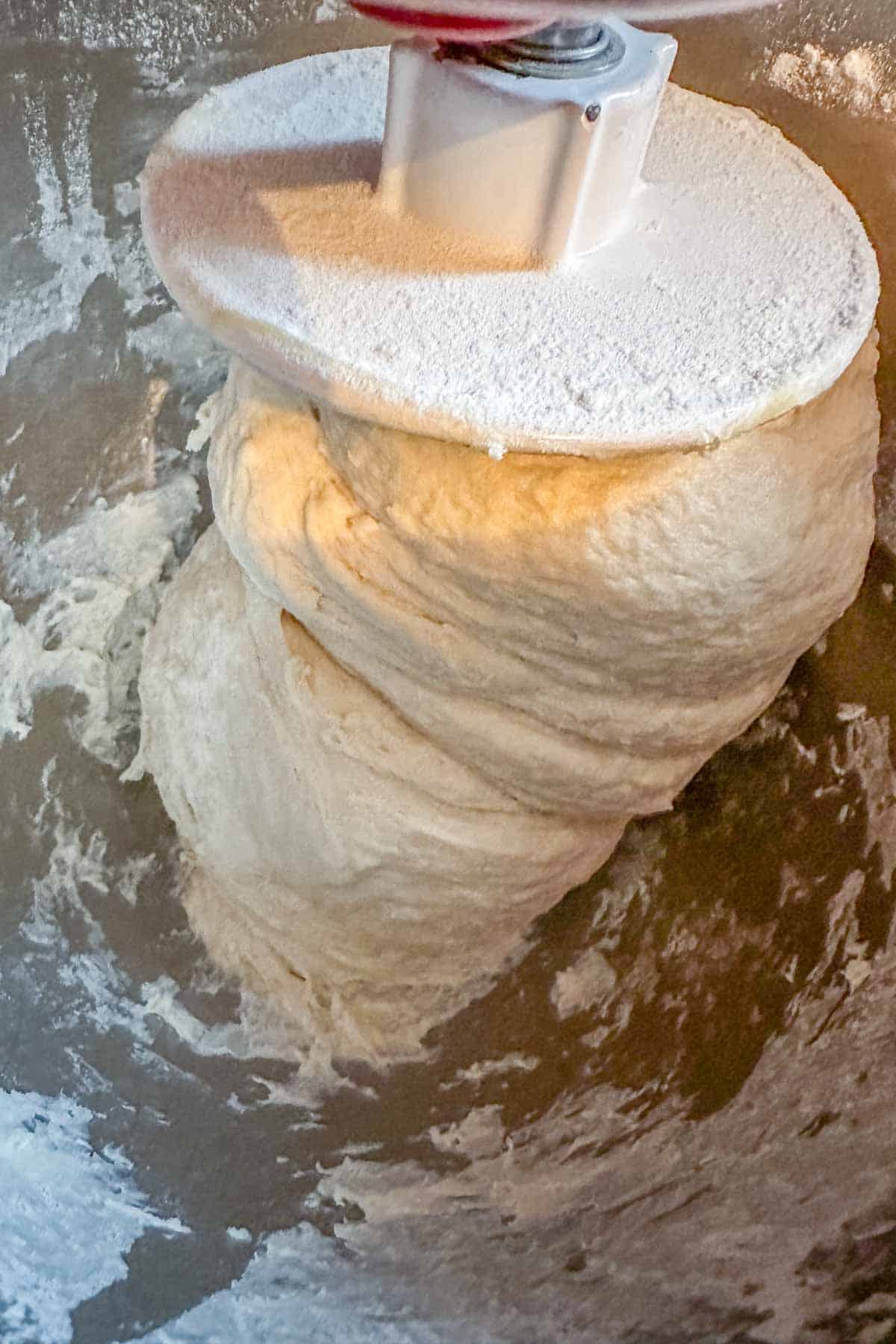 Bread dough in a stand mixer wrapped around dough hook.