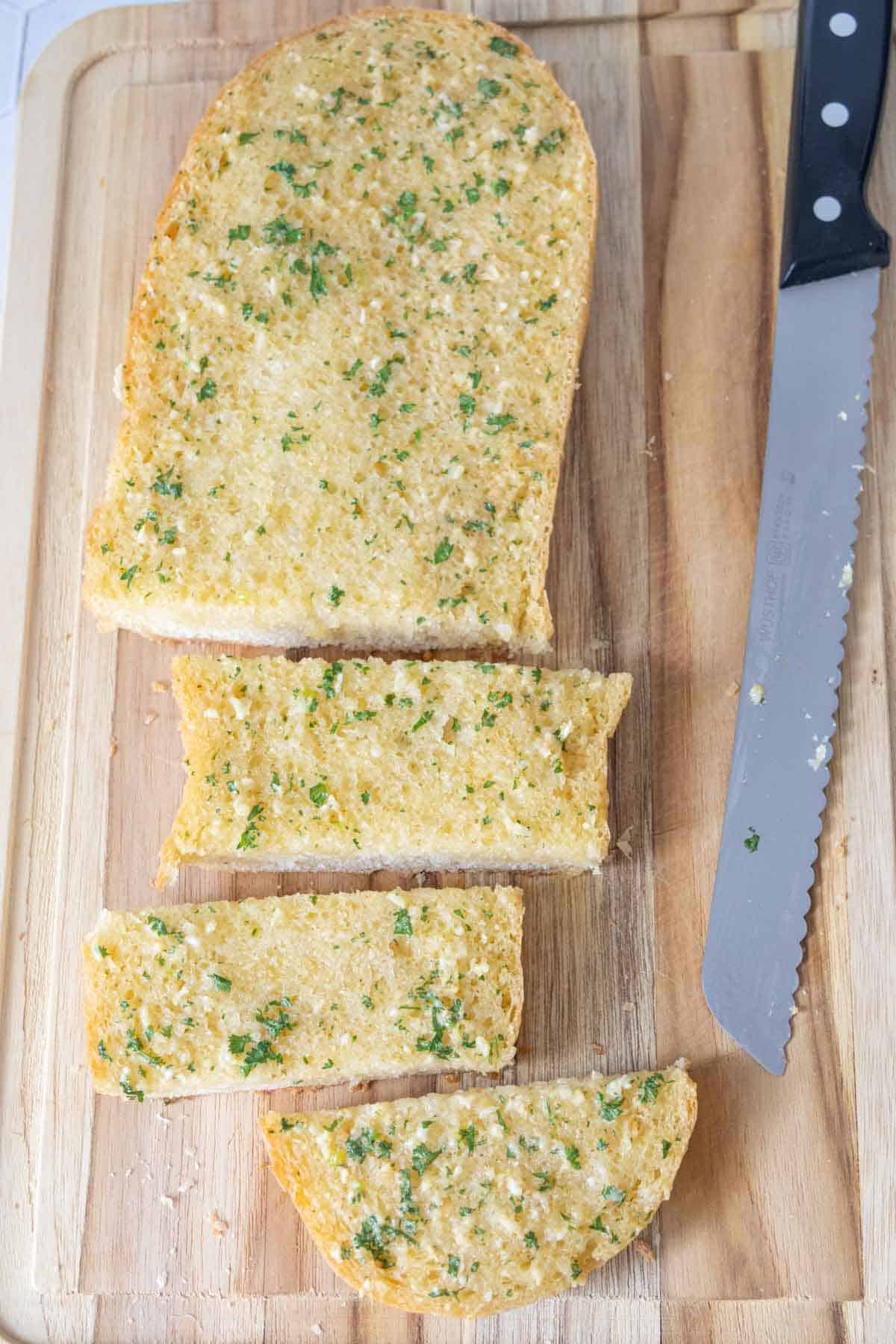 Overhead of homemade garlic bread partially cut into slices on a cutting board.