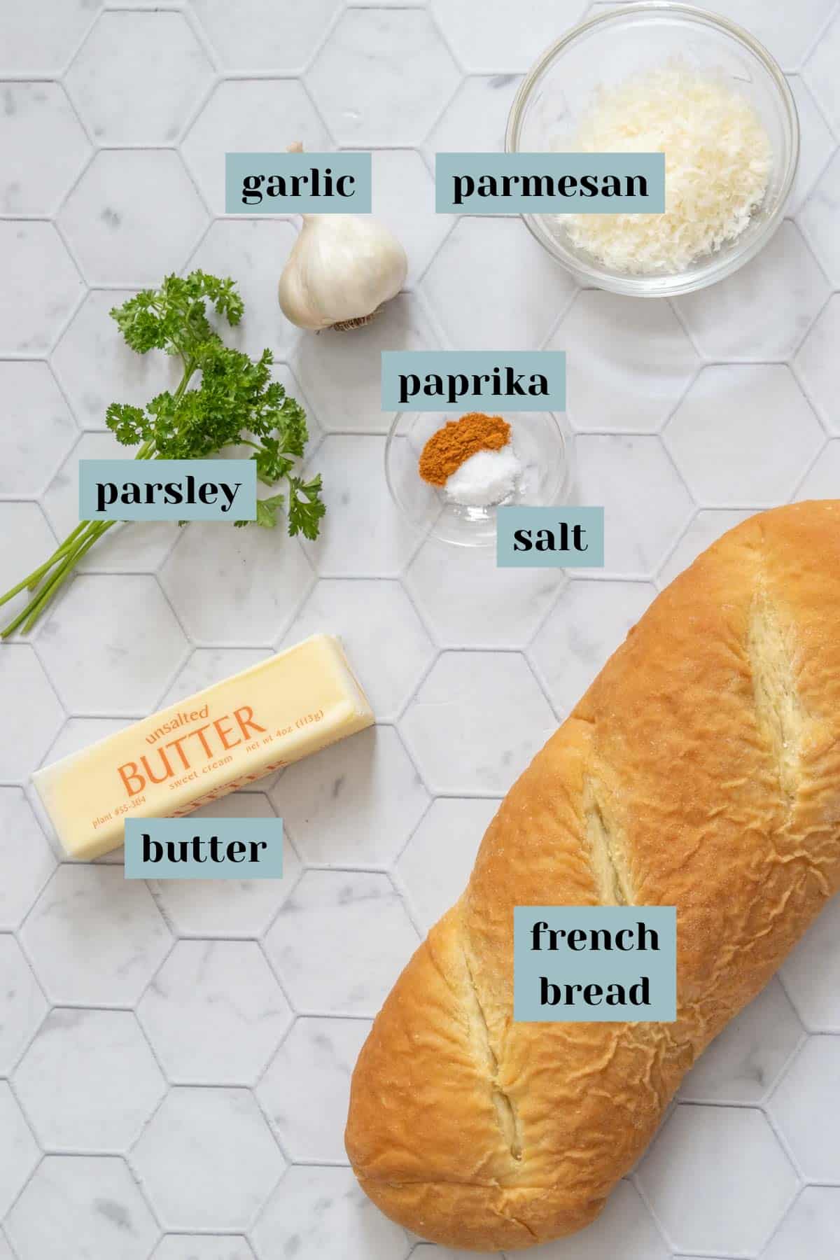Ingredients for homemade garlic bread on a tile surface with labels.