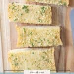 Four slices of homemade garlic bread with parsley rest on a wooden cutting board, shown from above.