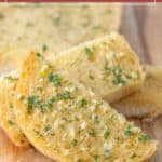 Slices of homemade garlic bread topped with chopped herbs are artfully arranged on a wooden surface.