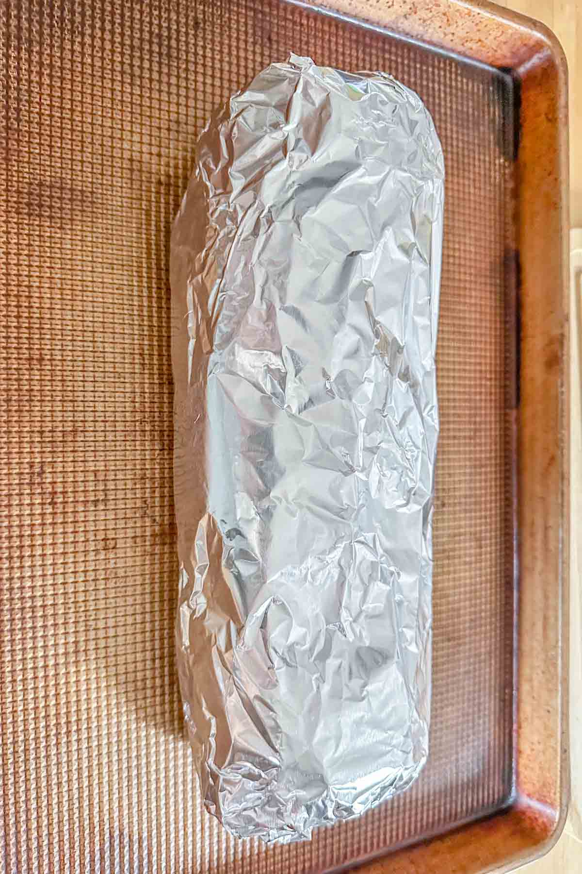 Loaf of garlic bread wrapped in foil on a baking sheet.