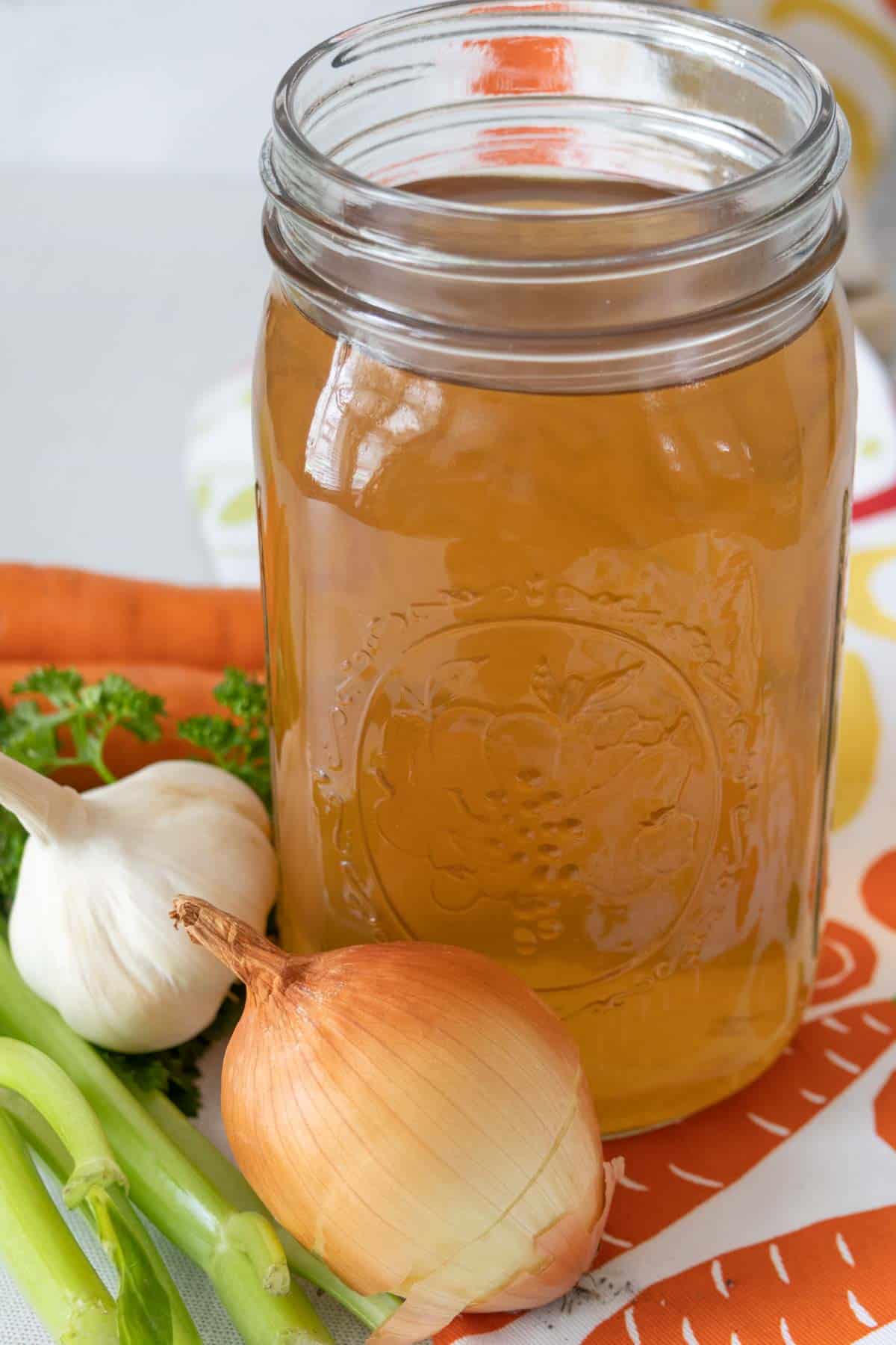 Open mason jar of homemade vegetable stock with veggies beside.