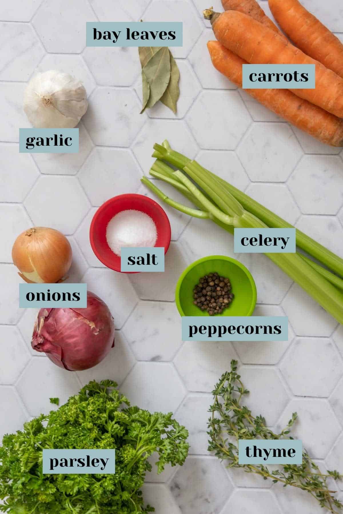 Ingredients for vegetable stock on a tile surface with labels.