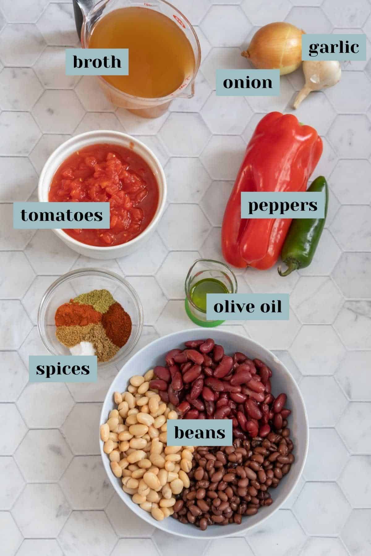 Ingredients for three bean chili on a tile surface with labels.