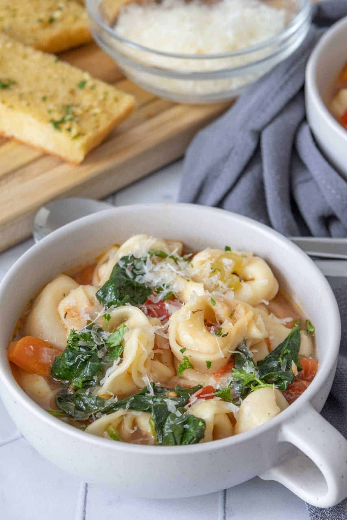 Low soup mug filled with tortellini soup topped with cheese.