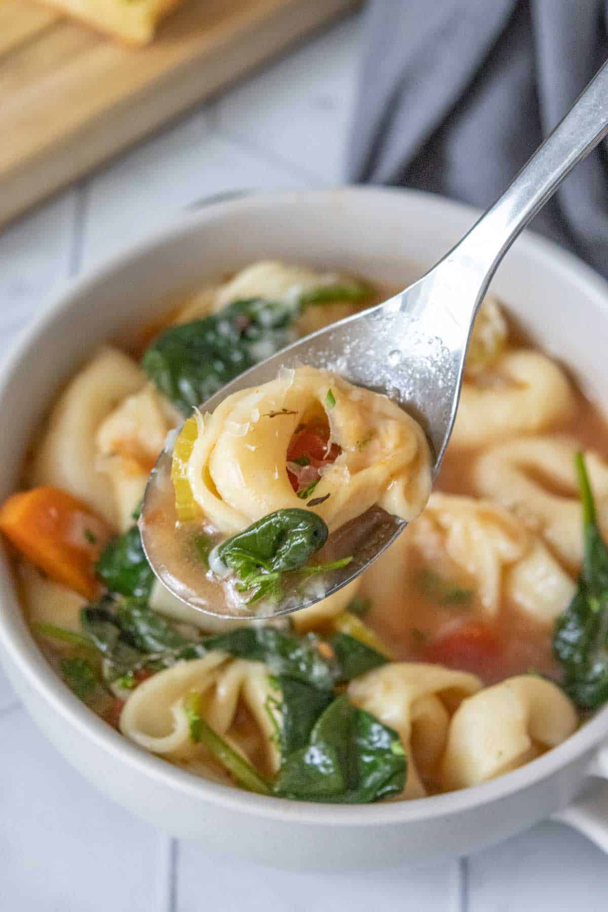 Spoonful of tortellini soup held over bowl.