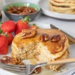 Pecan pancakes on a plate with a few pieces cut out and a fork in front.