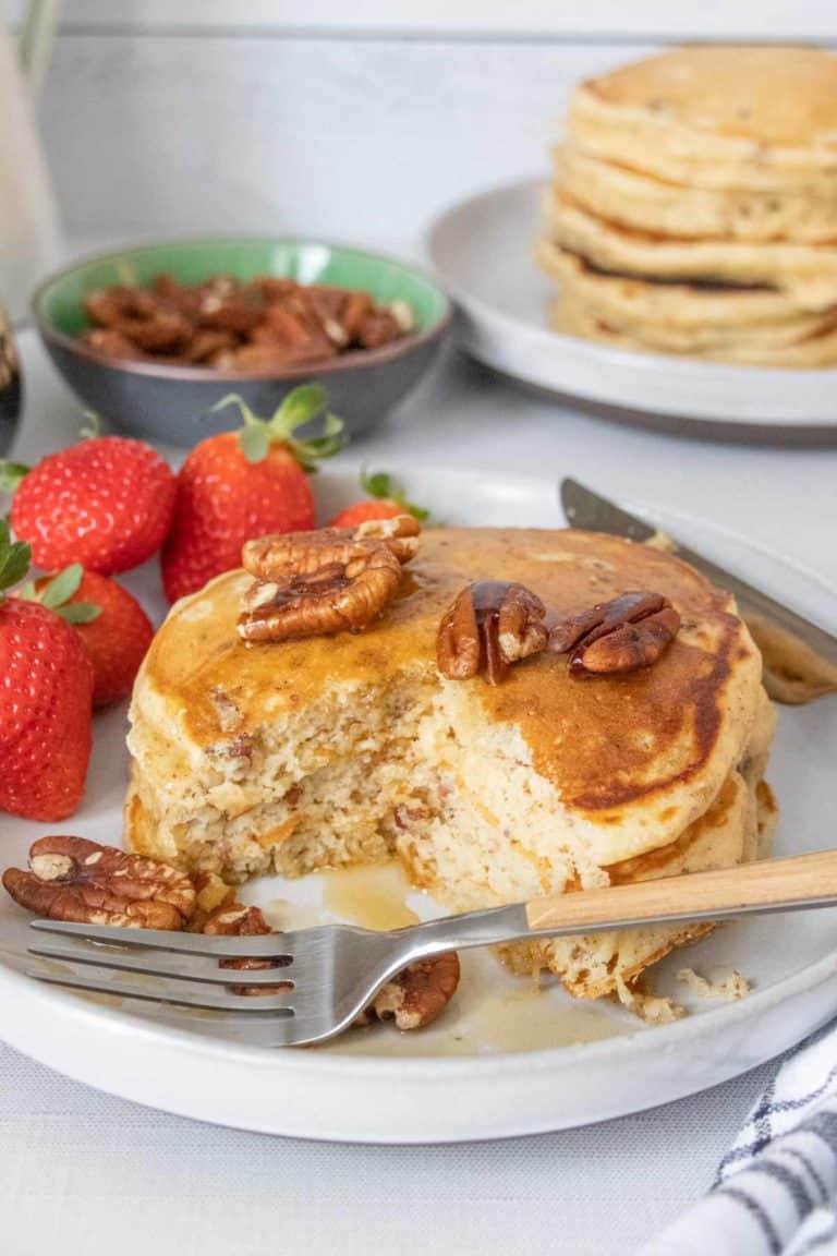 Pecan pancakes on a plate with a few pieces cut out and a fork in front.