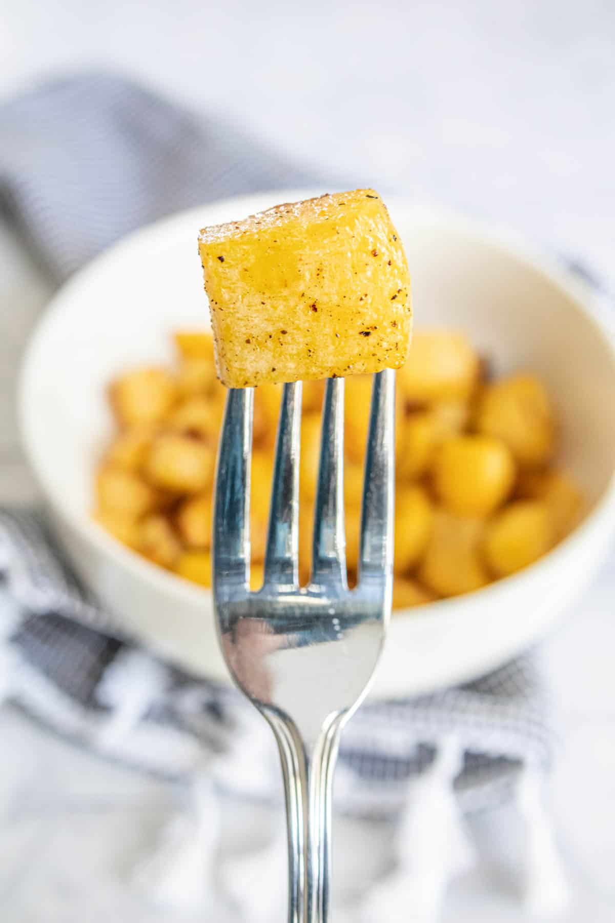 Fork holding up piece of roasted rutabaga.