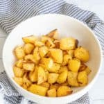 Roasted rutabaga in a white serving bowl with a black and white kitchen towel.