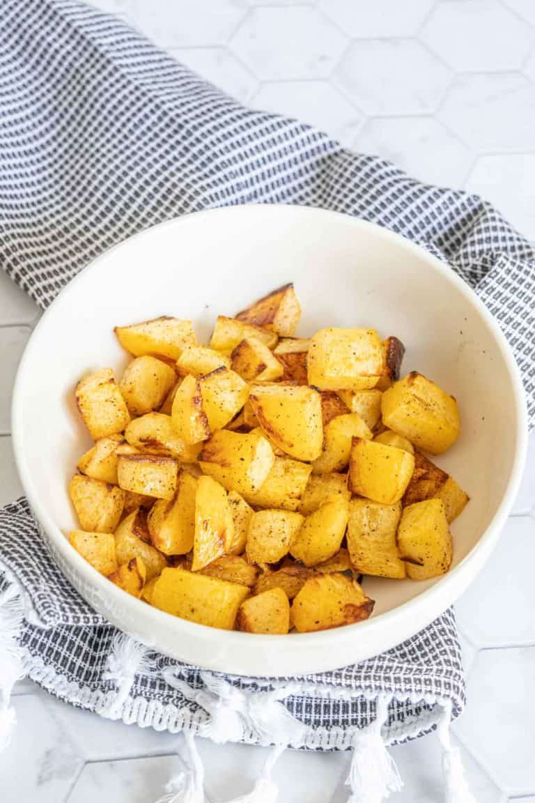 Roasted rutabaga in a white serving bowl with a black and white kitchen towel.