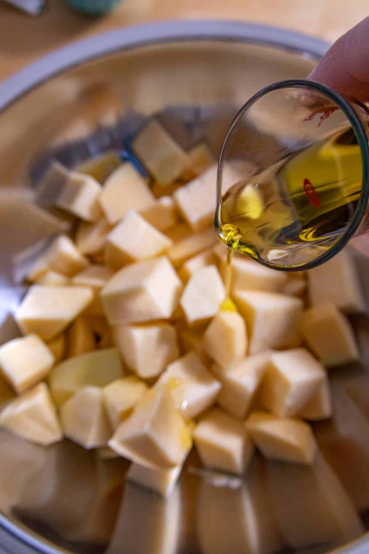 Olive oil being poured onto diced rutabaga in a bowl.