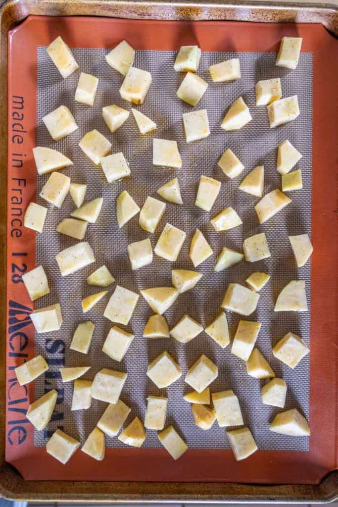Cubed potatoes and roasted rutabaga are spread out in a single layer on a silicone baking mat placed on a baking sheet, ready for roasting.