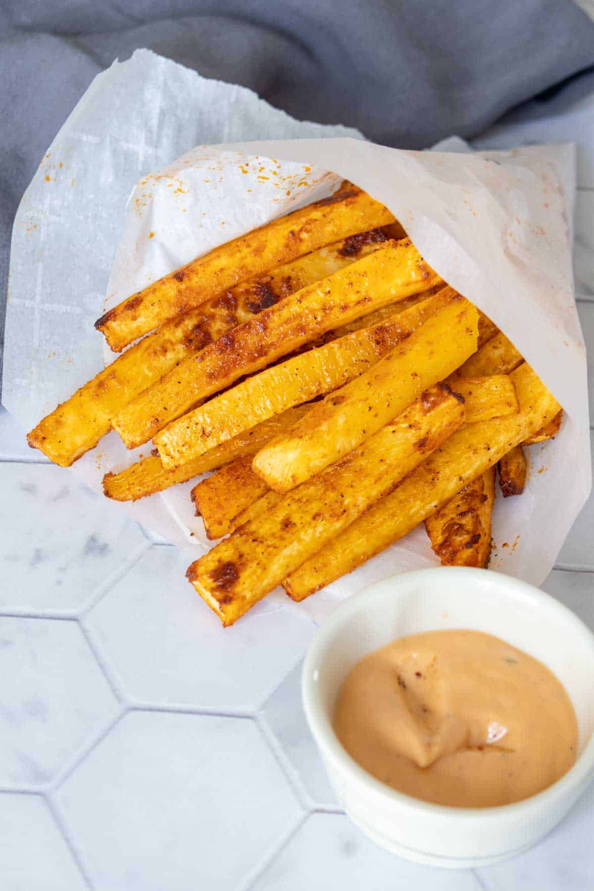 Rutabaga fries wrapped in a parchment bag with burger sauce in a bowl.