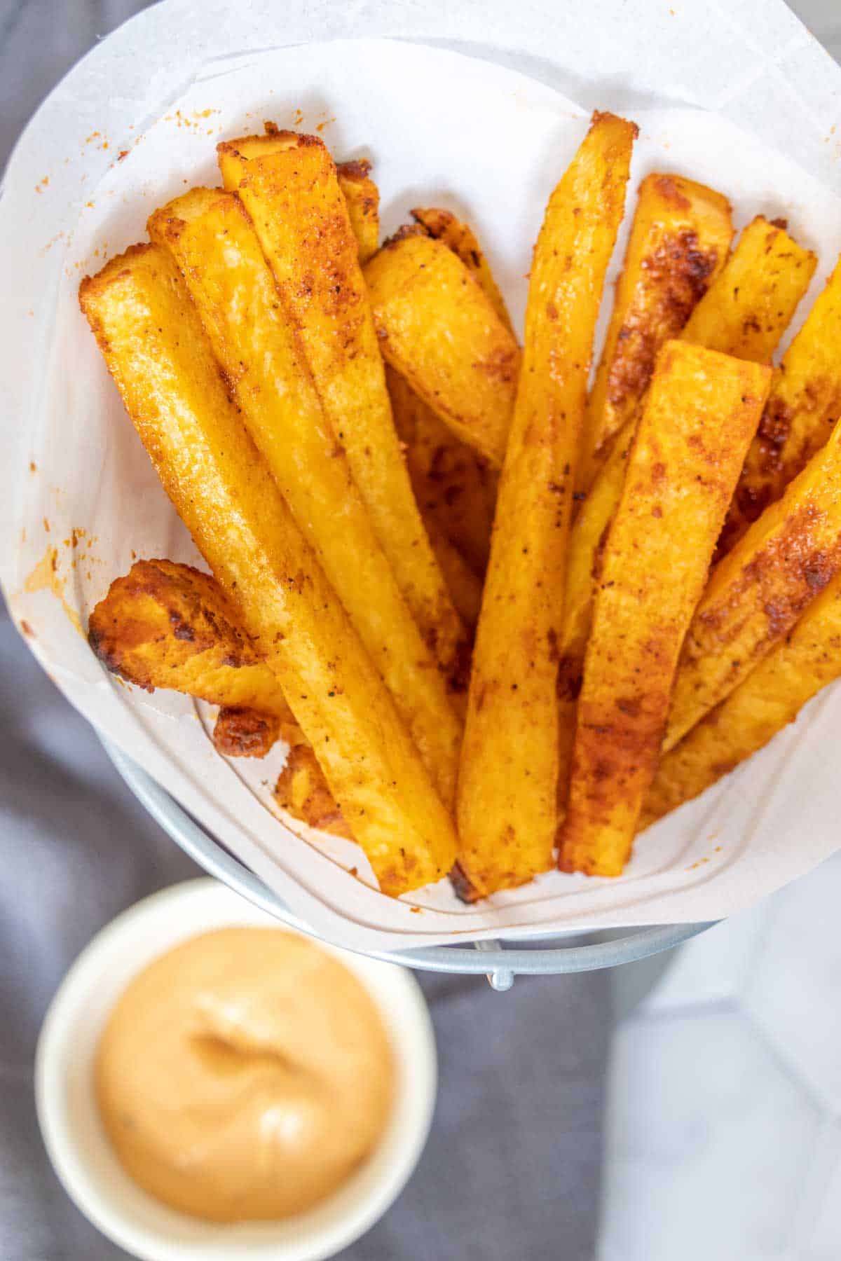 Overhead of rutabaga fries in a fry basket with burger sauce.