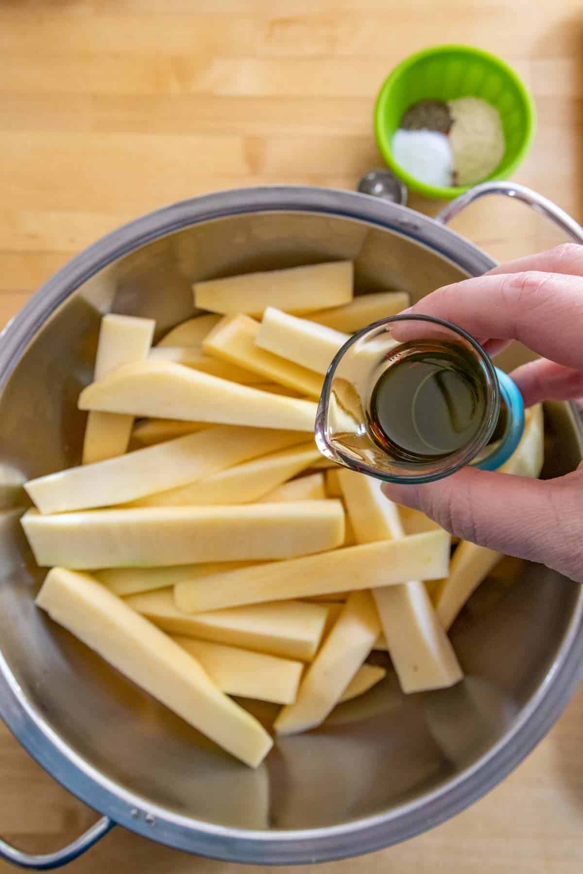 Pouring olive oil on rutabaga fries in a bowl.