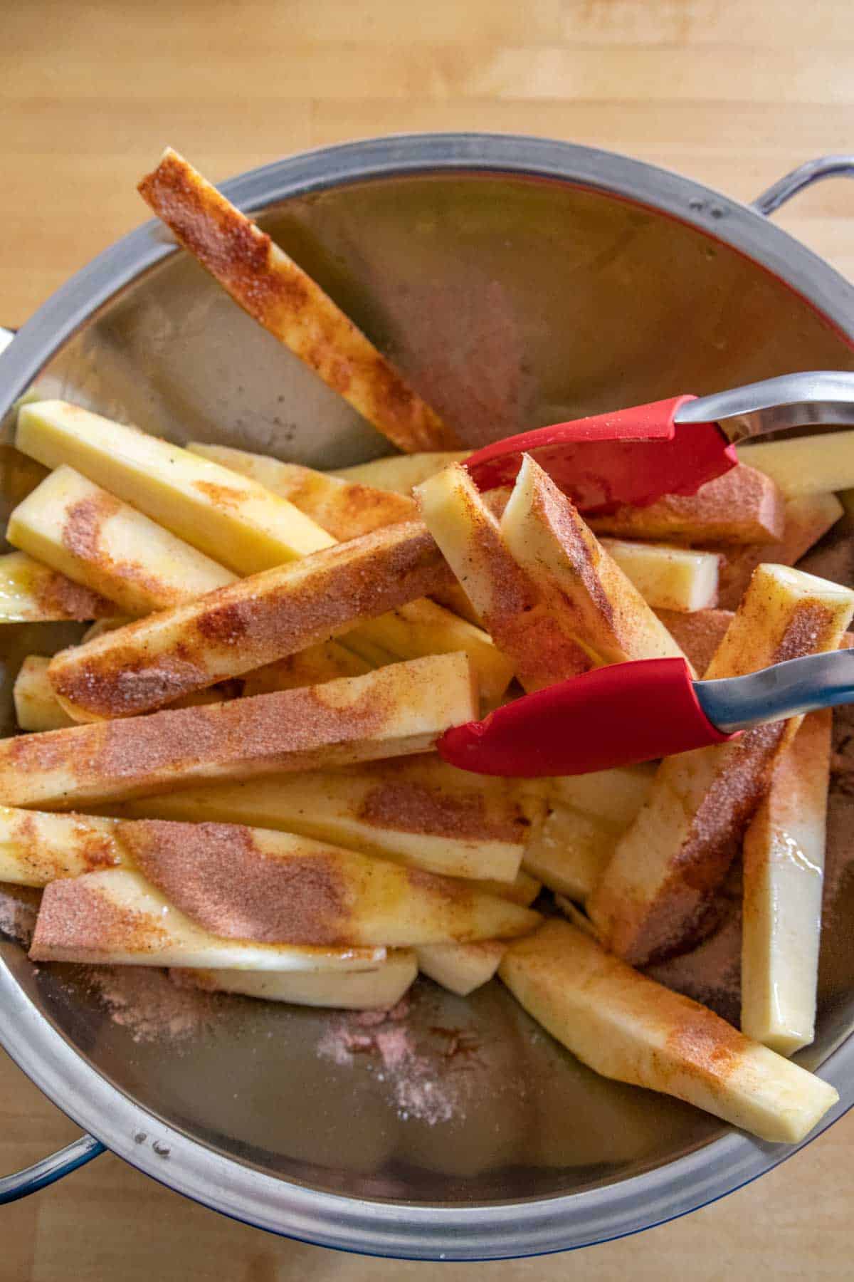 Tossing rutabaga fries with seasoning in a bowl.