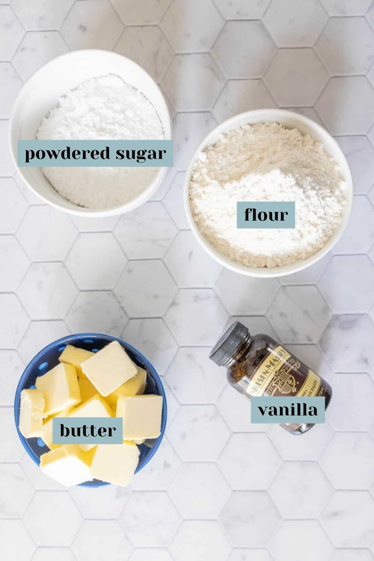 Ingredients for shortbread cookies on a tile surface with labels.